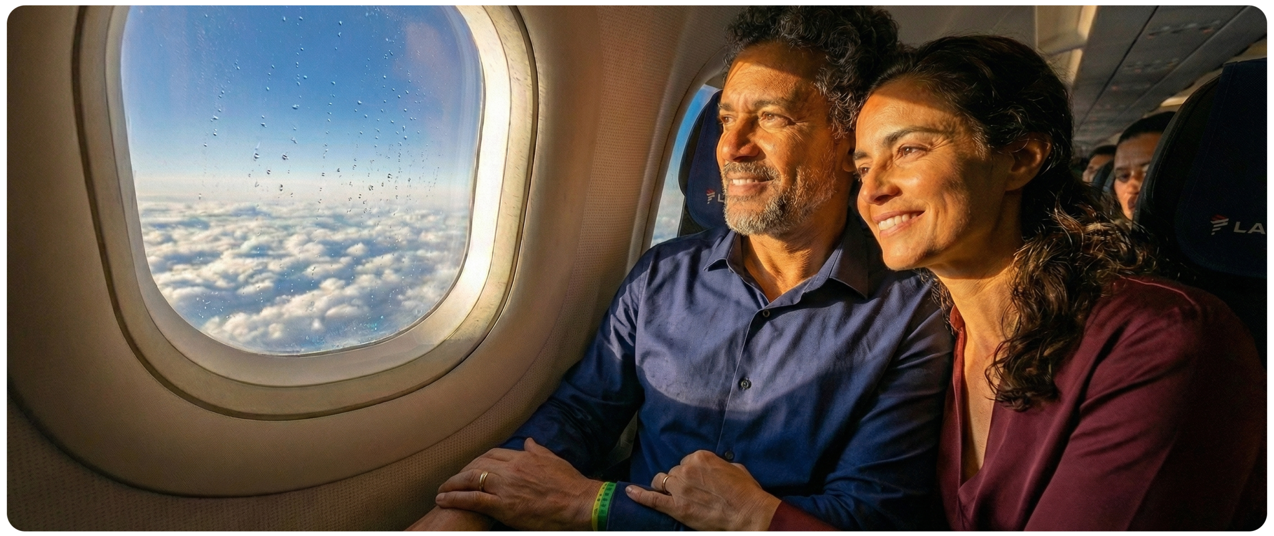 Casal sorrindo em avião, olhando a vista de nuvens pela janela.