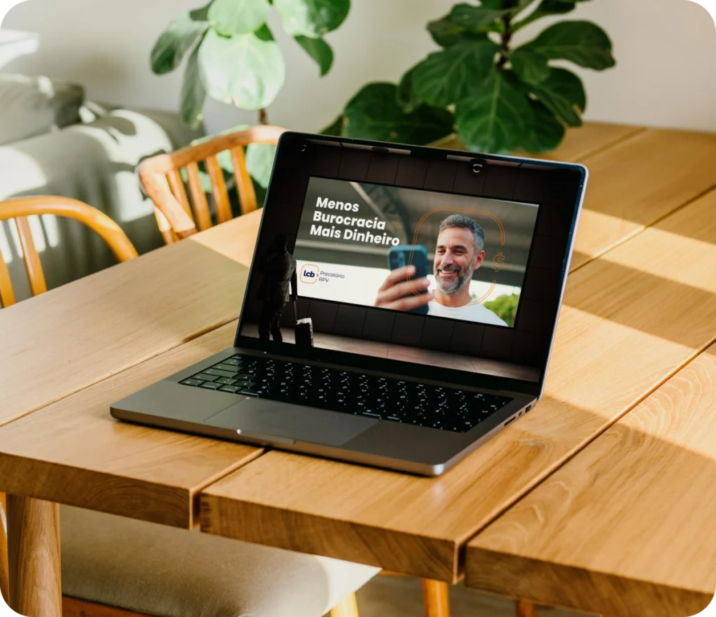 Laptop exibindo vídeo "Menos Burocracia Mais Dinheiro" com homem sorrindo. Solução digital para otimizar finanças.
